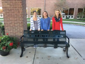 Lauren Eastman, Sydney Lindeman, and Sydney Watkins pose with a bench at Hospice of the Bluegrass that honors the service of the veterans staying there.