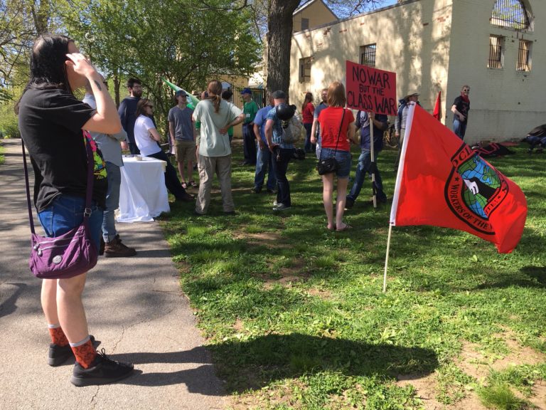 Crowd gathered in Duncan Park. Sign in the background reads “No War But The Class War”