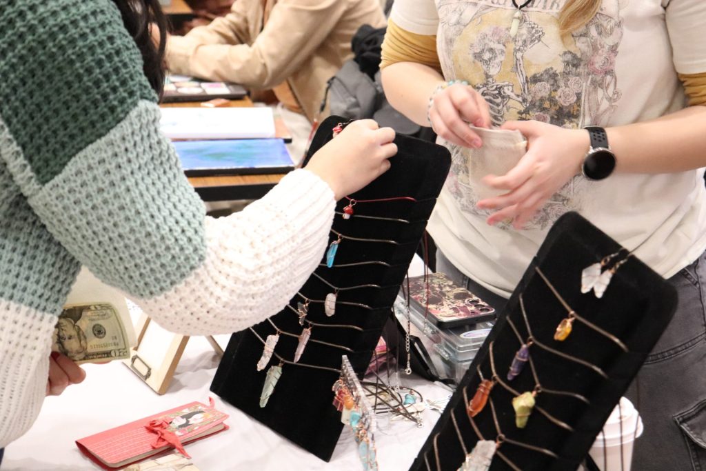 Patrons check out student Molly Uphoff's jewelry and crafts at the Maker's Market